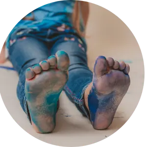 Niña con los pies pintados de azul y verde jugando en el suelo, actividad sensorial sin pantallas