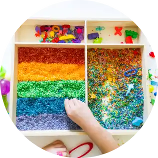 Bandeja sensorial con materiales de colores para niños, ideal para estimular los sentidos, la motricidad fina y la concentración a través del juego.
